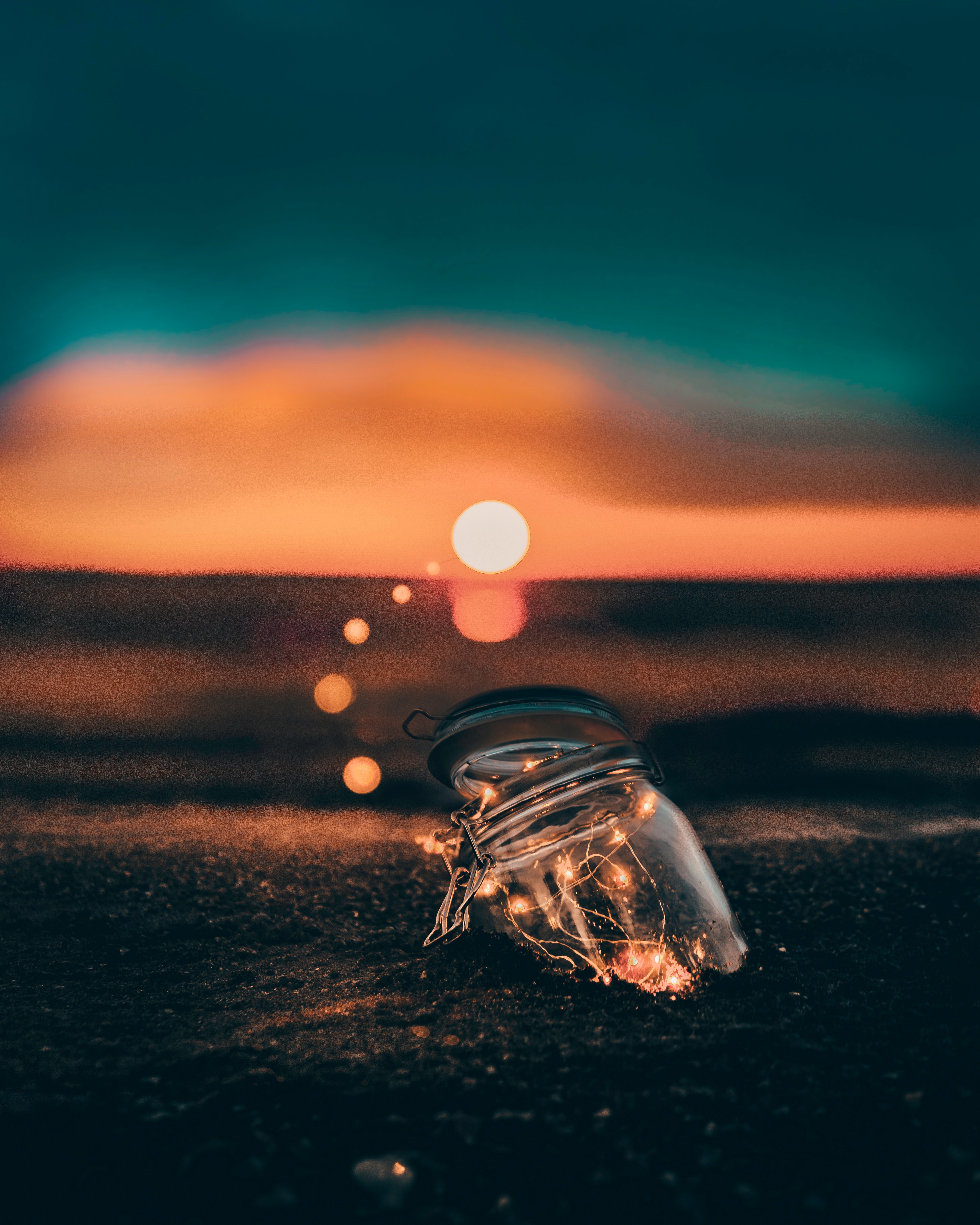 Jar with lights on sand at sunset